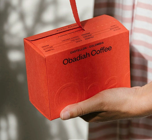 Red printed tear-apart slide-lid coffee box held by hand, with branding on front