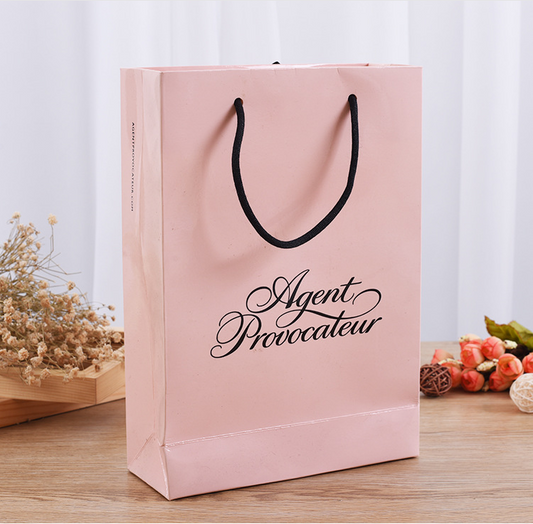 Matte pink paper shopping bag with black rope handles and Agent Provocateur logo