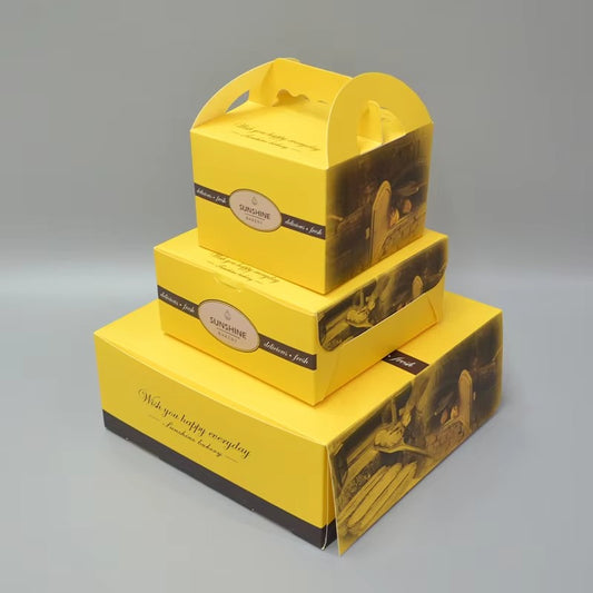 Stacked yellow printed cake boxes with handle cutout and clear window