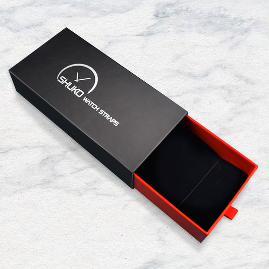 Black rigid drawer box with red inner and pull tab on marble background for watch straps