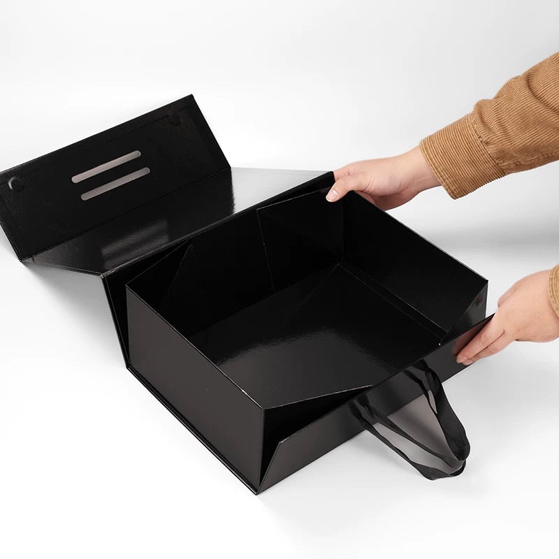 Black foldable gift box with ribbon handle, open showing the interior base