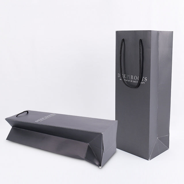 Black paper gift bag with twin rope handles; 'DEEP ROOTS' logo, angled view