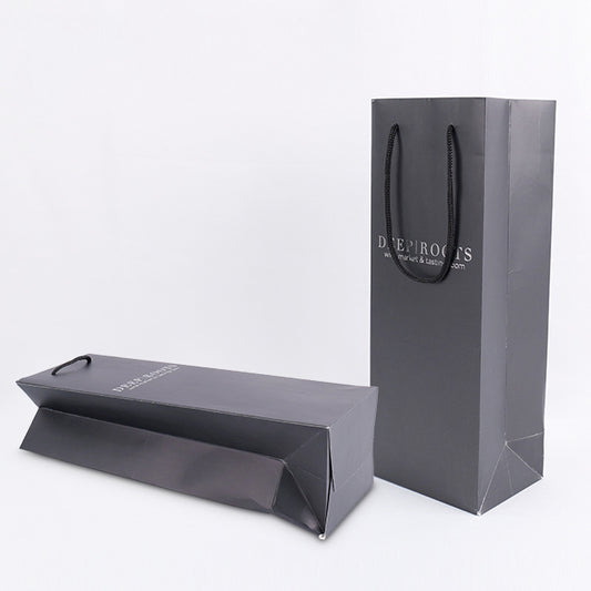 Black paper gift bag with twin rope handles; 'DEEP ROOTS' logo, angled view