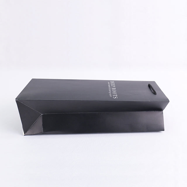 Black paper wine gift bag laid flat with rope handle detail and 'DEEP ROOTS' text