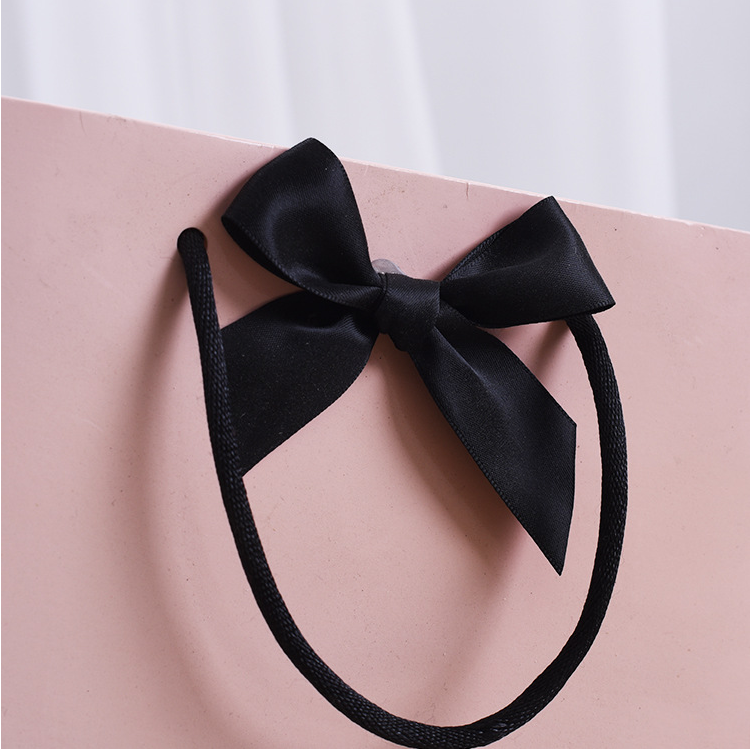 Black satin bow hair accessory styled with custom pink luxury shopping bag