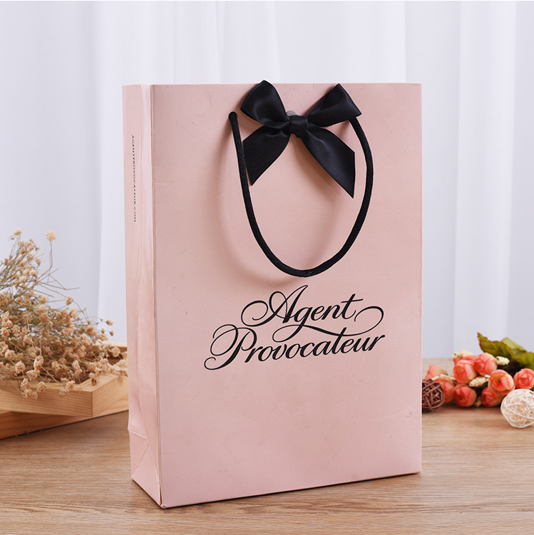 Custom pink paper bag with black bow-tied rope handles and elegant script logo