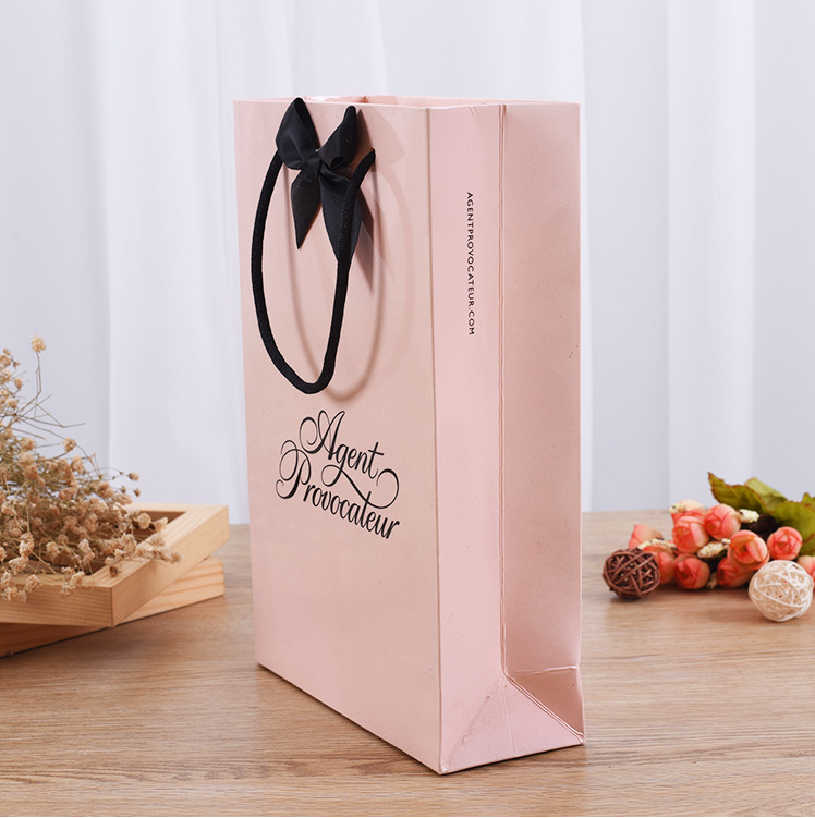 Side view of pink brand bag with bow handle and website URL printed on edge