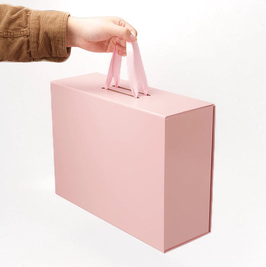 Pink foldable gift box with ribbon handle, lifted by a hand
