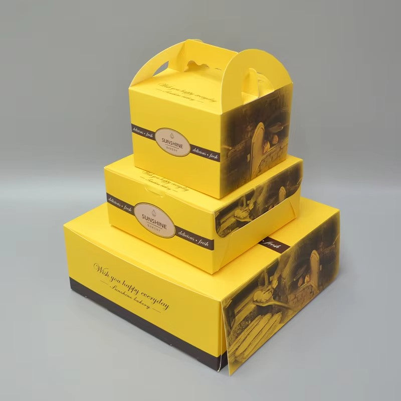 Stacked yellow printed cake boxes with handle cutout and clear window
