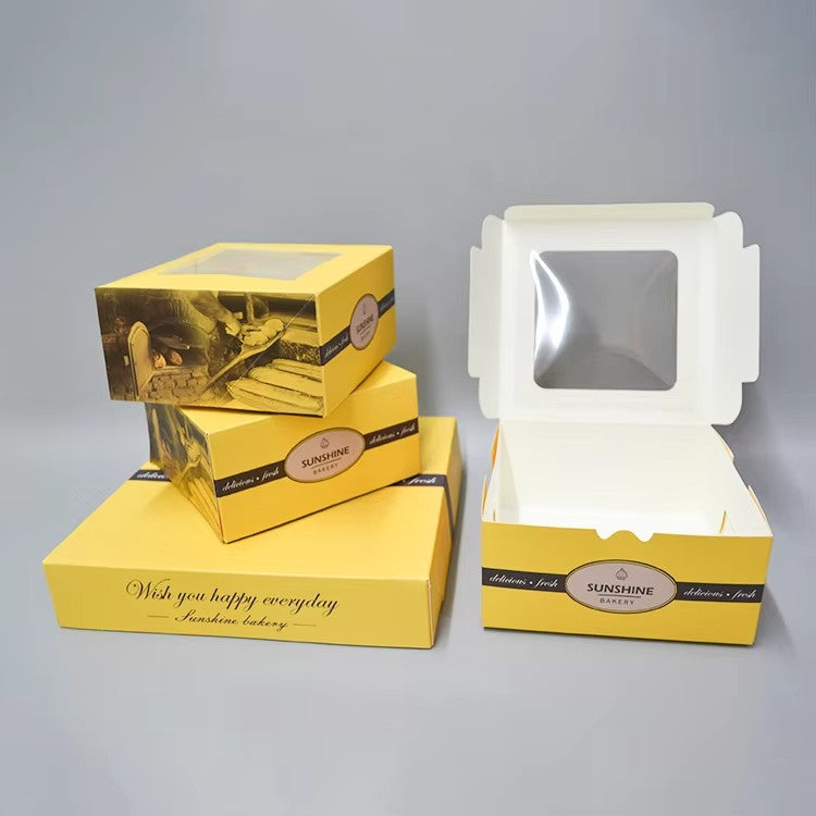Open white cake box with clear window and handle, with stacked yellow boxes